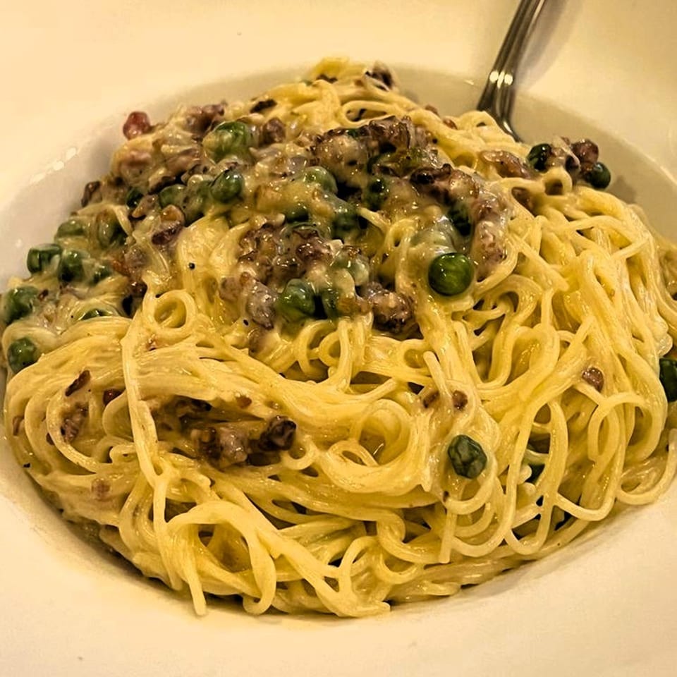 Close-up of spaghetti carbonara with peas and bacon in a white bowl at Viva Italiano Pizzeria.