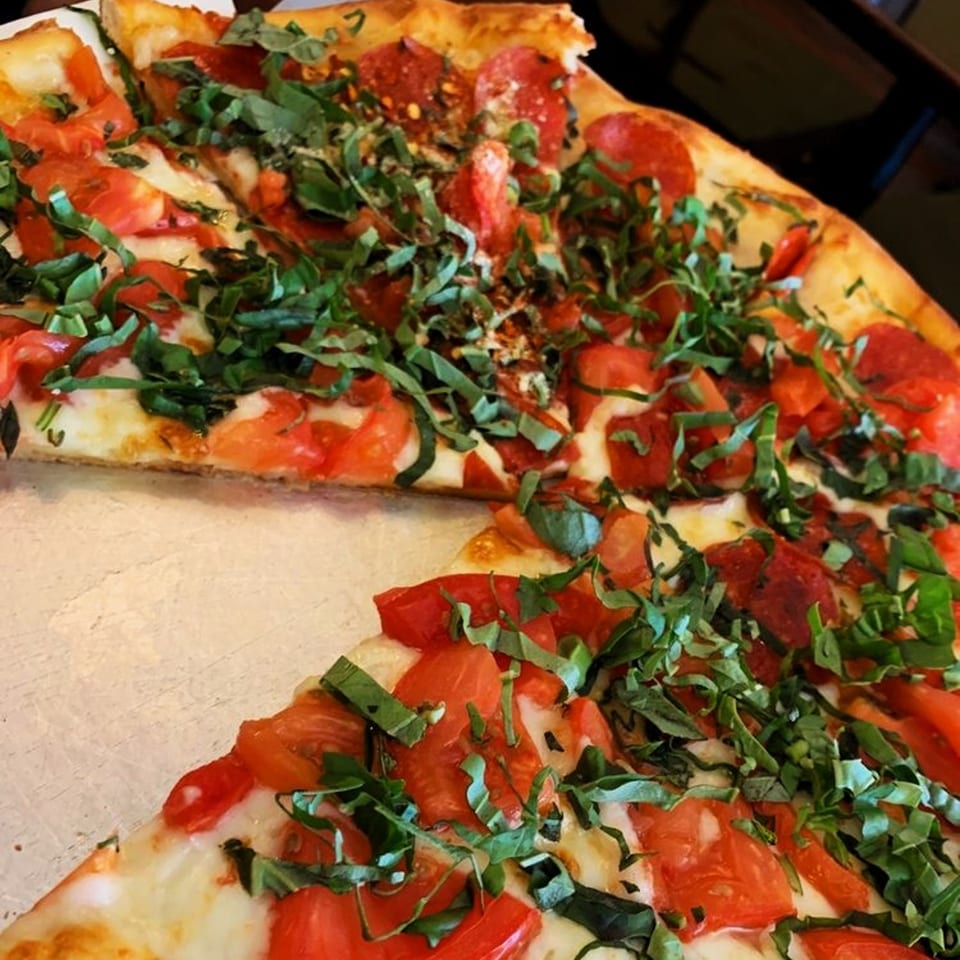 A Viva Italiano Pizzeria pizza with pepperoni, diced tomatoes, fresh basil, and red pepper flakes.