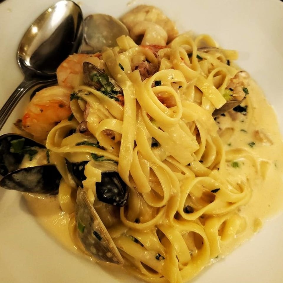 Creamy seafood fettuccine with mussels, shrimp, and clams, served on a white plate with spoons.