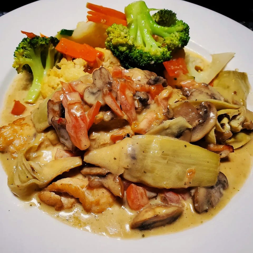 Italian chicken dish with creamy sauce, mushrooms, artichokes, tomatoes, and a side of broccoli and carrots.
